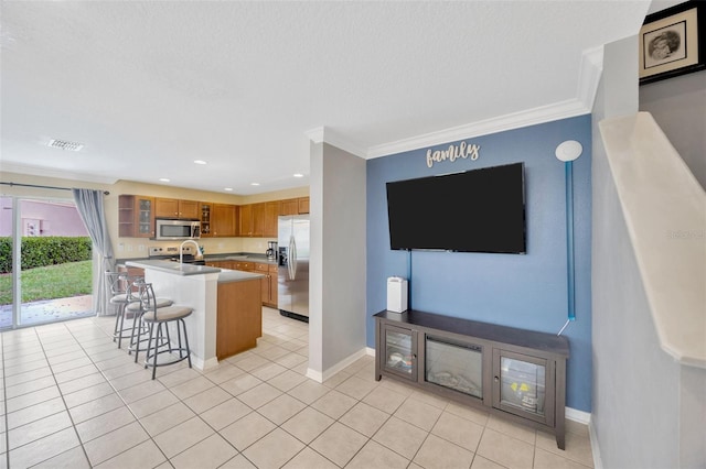 kitchen with light tile patterned floors, stainless steel appliances, visible vents, a kitchen breakfast bar, and ornamental molding