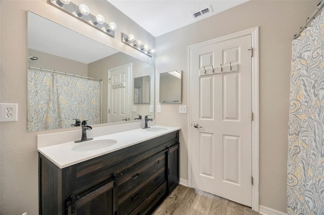 full bathroom featuring double vanity, wood finished floors, a sink, and visible vents