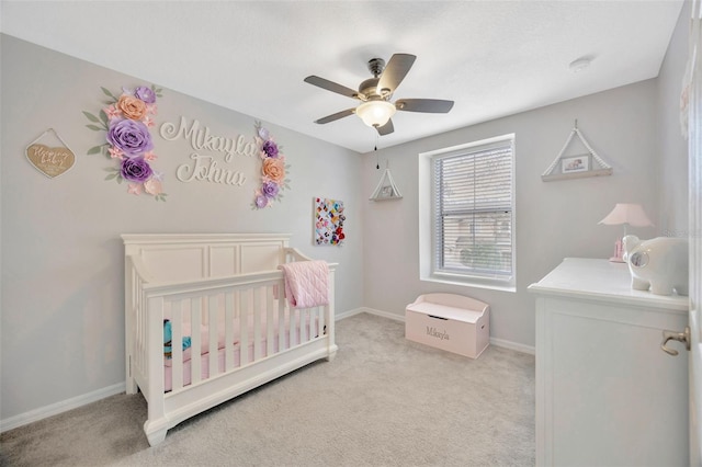 bedroom featuring baseboards, a crib, a ceiling fan, and light colored carpet