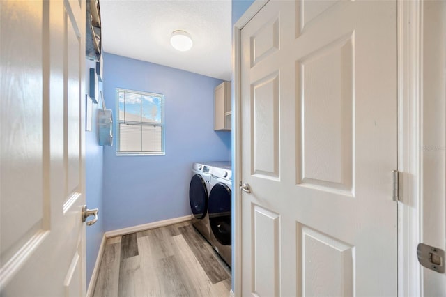 clothes washing area with light wood-style flooring, independent washer and dryer, cabinet space, and baseboards