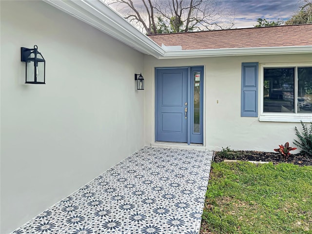 view of exterior entry with roof with shingles and stucco siding