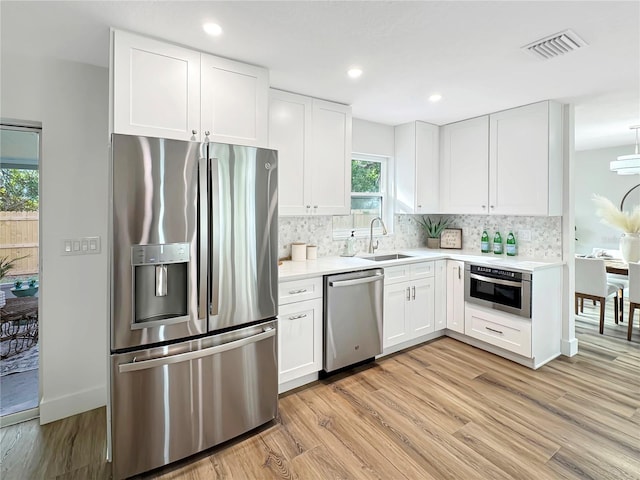 kitchen featuring a sink, visible vents, appliances with stainless steel finishes, light wood-type flooring, and decorative backsplash