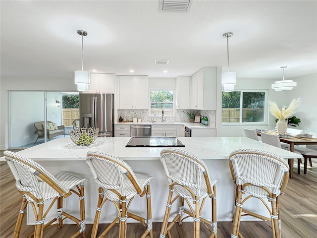 kitchen featuring stainless steel appliances, a sink, visible vents, light wood finished floors, and tasteful backsplash