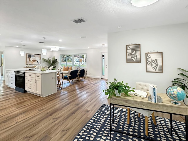 interior space with range with electric cooktop, wood finished floors, visible vents, white cabinetry, and open floor plan