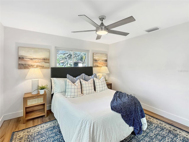 bedroom featuring a ceiling fan, baseboards, visible vents, and wood finished floors