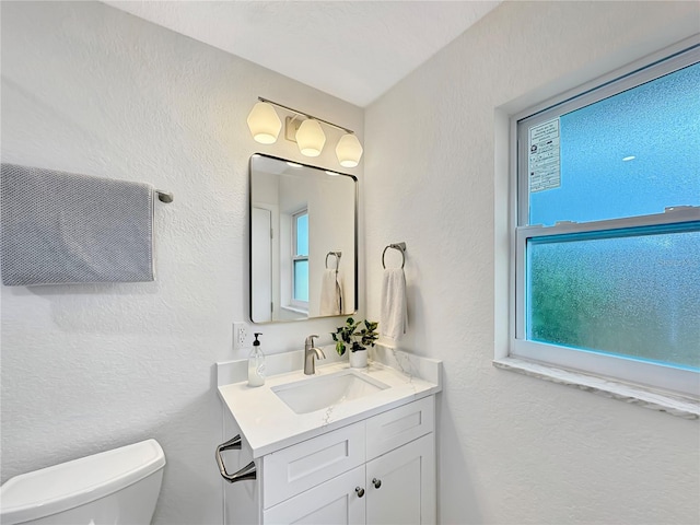 bathroom featuring a textured wall, vanity, and toilet