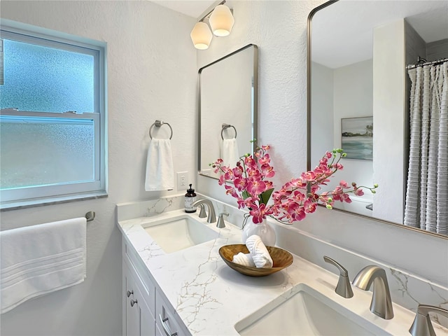 full bathroom with a textured wall, a sink, and double vanity