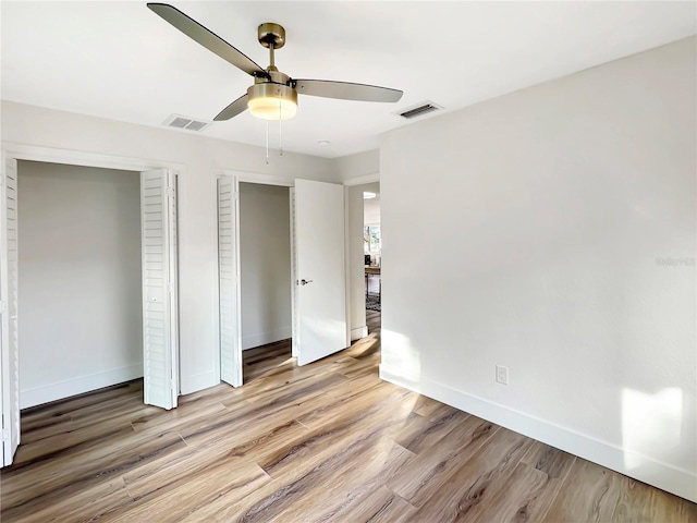 unfurnished bedroom featuring multiple closets, visible vents, ceiling fan, wood finished floors, and baseboards