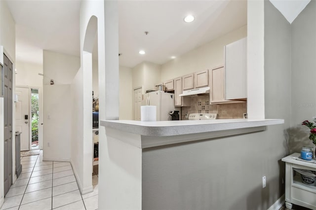 kitchen featuring under cabinet range hood, a peninsula, light countertops, freestanding refrigerator, and tasteful backsplash