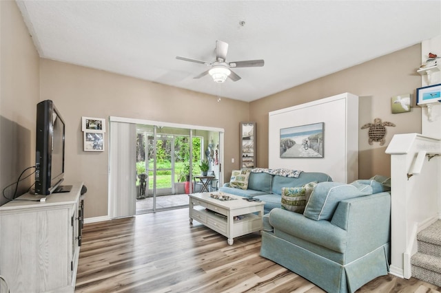 living area featuring stairs, baseboards, light wood-style flooring, and a ceiling fan