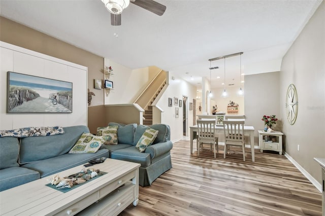 living area featuring ceiling fan, stairway, light wood-type flooring, and baseboards