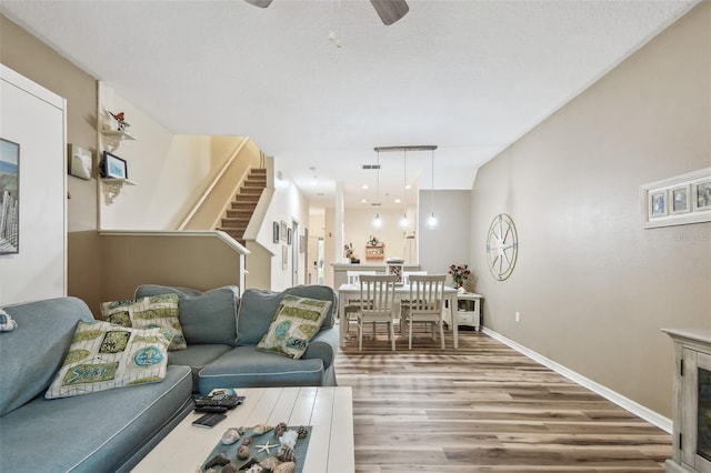 living area featuring stairs, ceiling fan, baseboards, and wood finished floors