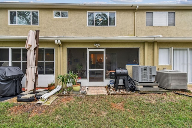 back of property with a sunroom, a lawn, central AC, and stucco siding