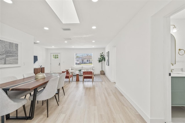 dining area featuring light wood finished floors, a skylight, visible vents, baseboards, and recessed lighting