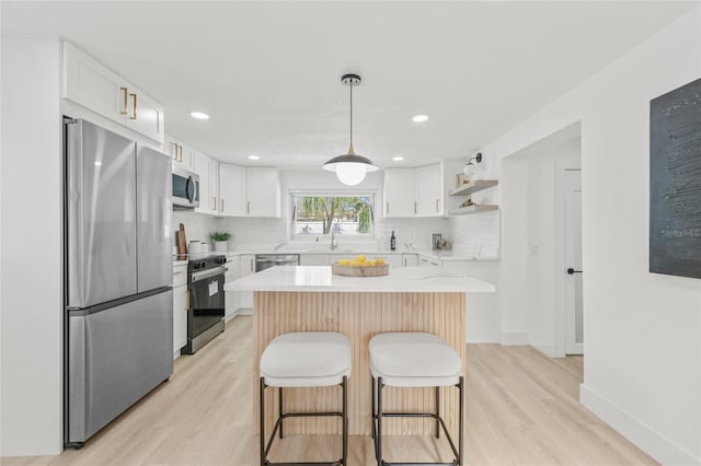 kitchen with appliances with stainless steel finishes, a breakfast bar, light countertops, white cabinetry, and backsplash