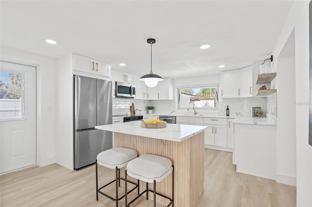 kitchen with open shelves, light wood-style flooring, appliances with stainless steel finishes, white cabinetry, and a kitchen breakfast bar