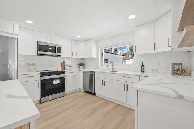 kitchen featuring light stone counters, appliances with stainless steel finishes, white cabinets, a sink, and light wood-type flooring