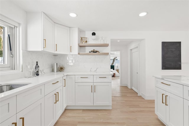 kitchen with open shelves, tasteful backsplash, light wood-style floors, white cabinetry, and light stone countertops