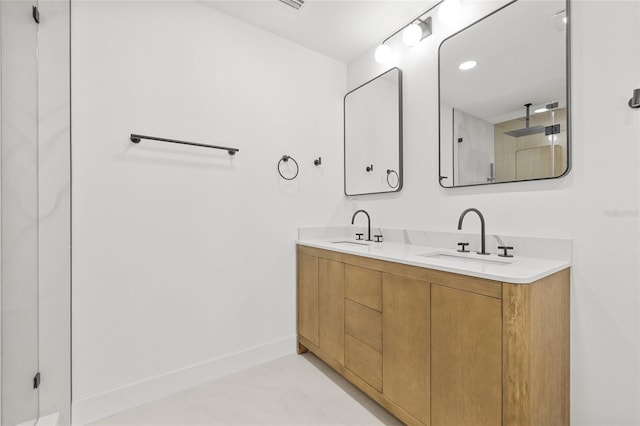 full bath with double vanity, walk in shower, a sink, and baseboards