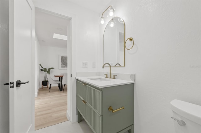 bathroom with a skylight, vanity, toilet, and wood finished floors