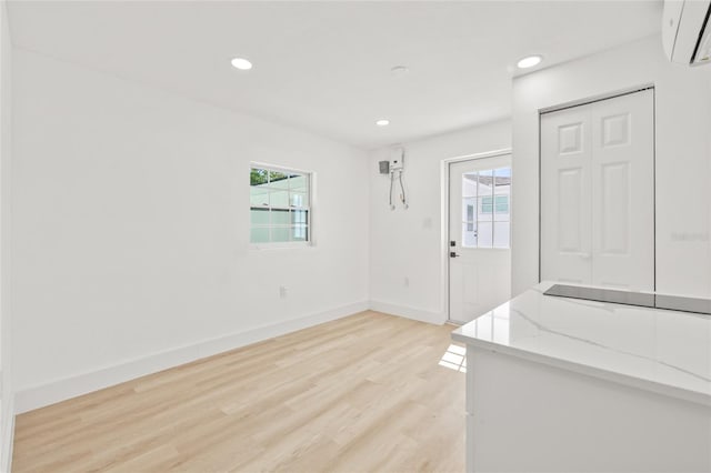 unfurnished dining area featuring a wealth of natural light, a wall unit AC, light wood-style flooring, and baseboards