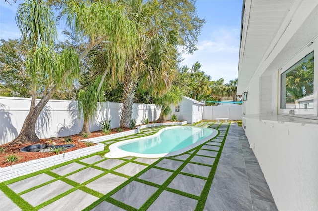 view of swimming pool featuring a fenced backyard, an outdoor structure, a fenced in pool, a storage unit, and a patio area