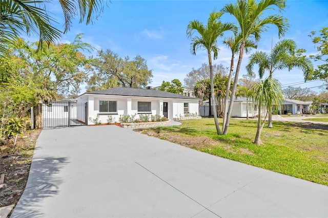 ranch-style home featuring concrete driveway, a gate, fence, a front yard, and stucco siding