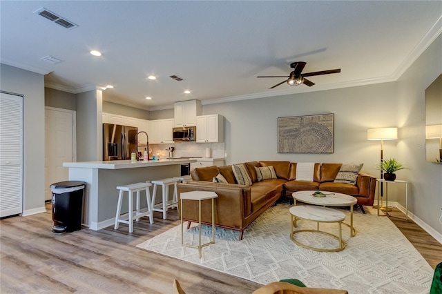 living room with baseboards, light wood-type flooring, visible vents, and crown molding