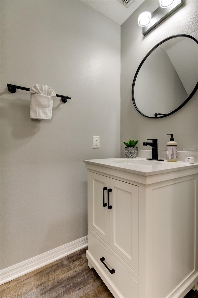 bathroom with visible vents, vanity, baseboards, and wood finished floors