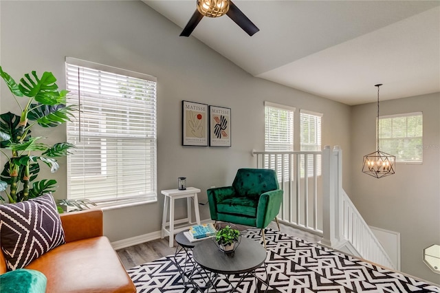 sitting room featuring light wood finished floors, lofted ceiling, an upstairs landing, baseboards, and ceiling fan with notable chandelier