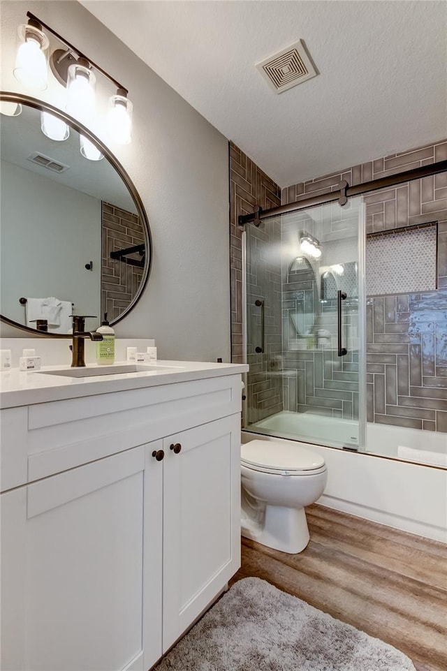 full bath with toilet, visible vents, combined bath / shower with glass door, and wood finished floors