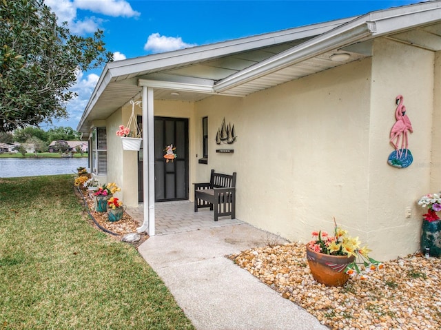 doorway to property with a water view, a lawn, and stucco siding