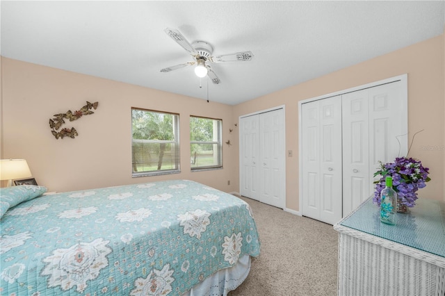 bedroom with light carpet, baseboards, a ceiling fan, and multiple closets