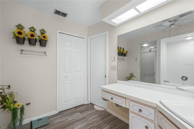 bathroom with a shower with shower door, a skylight, wood finished floors, visible vents, and vanity