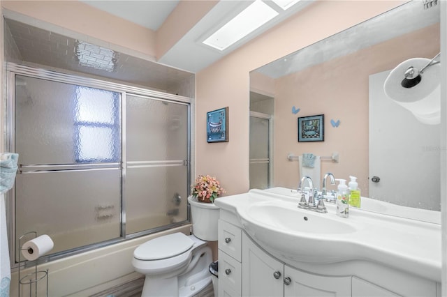 bathroom with toilet, a skylight, combined bath / shower with glass door, and vanity