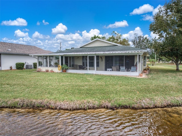 rear view of property with a shingled roof, central AC unit, a sunroom, a water view, and a yard