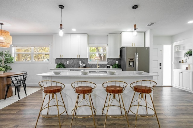 kitchen featuring a breakfast bar, visible vents, stainless steel fridge with ice dispenser, and white cabinetry