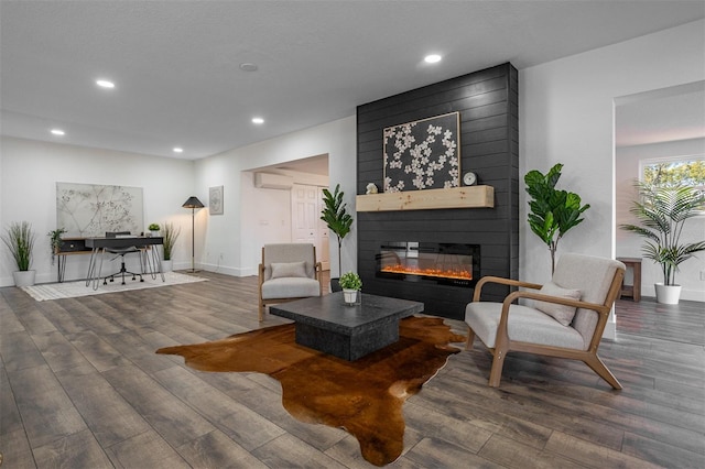 living area featuring a wall unit AC, recessed lighting, a fireplace, wood finished floors, and baseboards