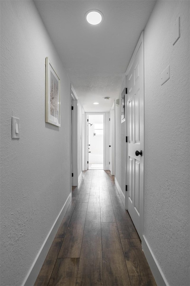 hall with dark wood-style floors, a textured wall, and baseboards