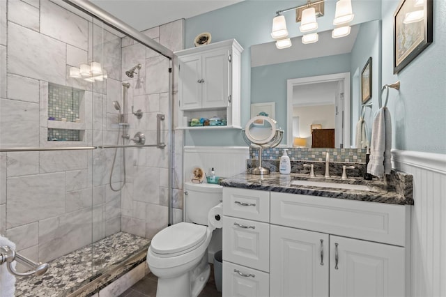 full bath featuring toilet, a stall shower, vanity, and wainscoting