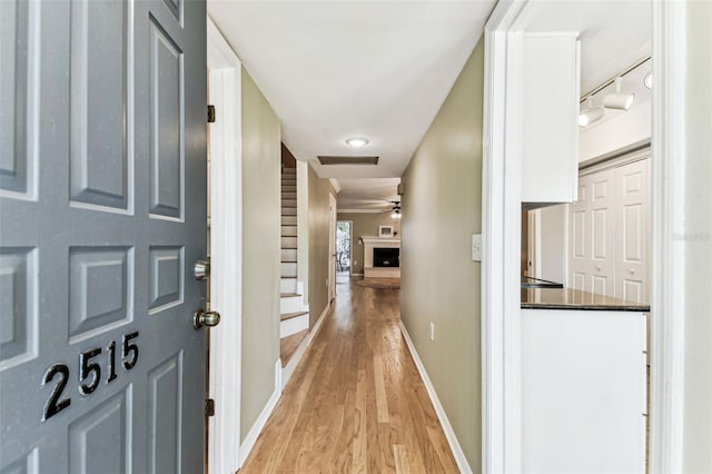 corridor with track lighting, baseboards, and light wood finished floors