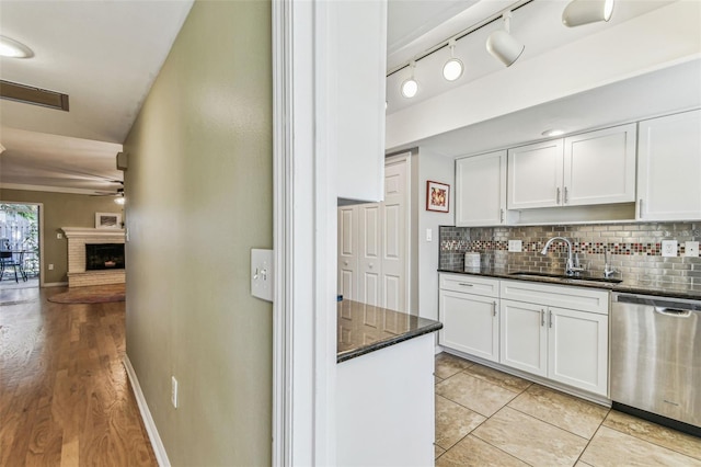 kitchen featuring a sink, white cabinetry, stainless steel dishwasher, a brick fireplace, and decorative backsplash