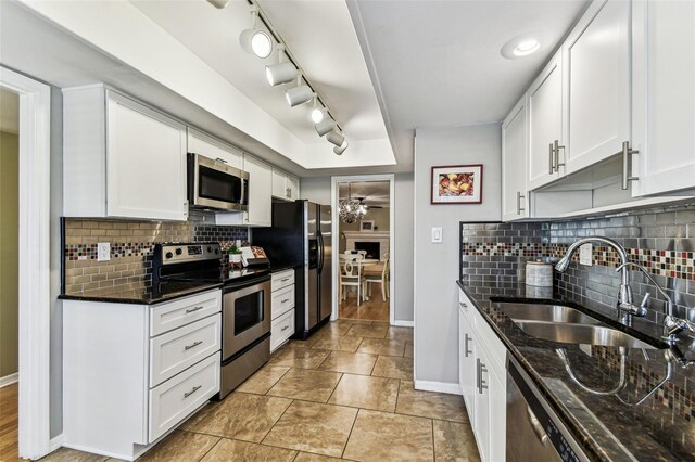 kitchen with stainless steel appliances, white cabinetry, a sink, and dark stone countertops