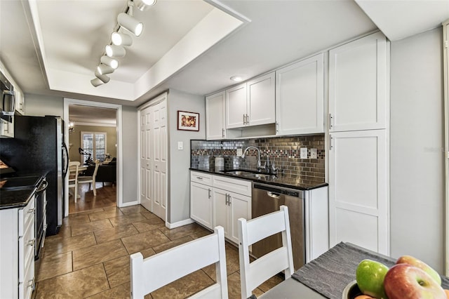 kitchen with dark countertops, a raised ceiling, a sink, and stainless steel dishwasher