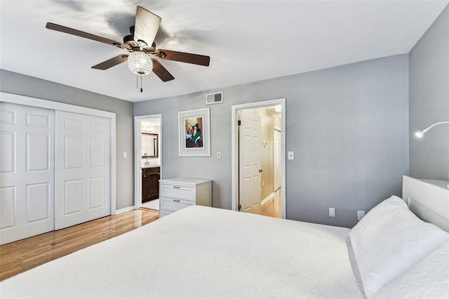 bedroom with a ceiling fan, visible vents, light wood-style floors, a closet, and ensuite bath