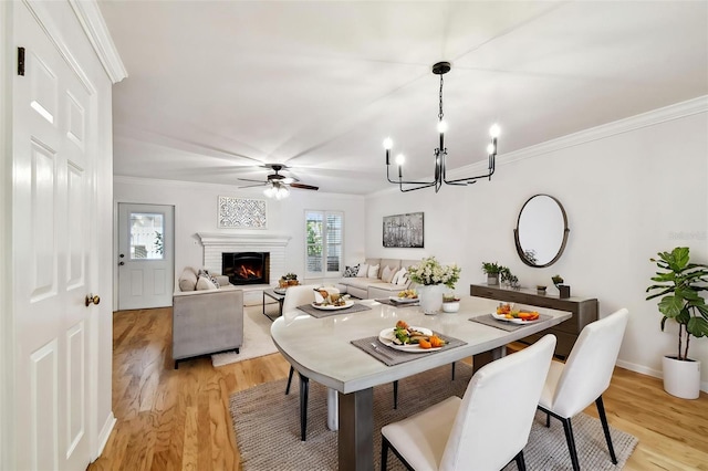 dining room featuring light wood-style floors, crown molding, a chandelier, a fireplace, and a ceiling fan