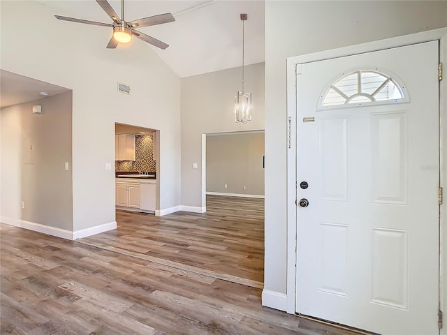 entrance foyer featuring high vaulted ceiling, ceiling fan with notable chandelier, wood finished floors, visible vents, and baseboards