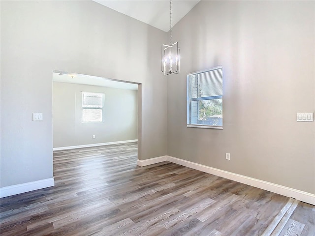 empty room featuring baseboards, high vaulted ceiling, a chandelier, and wood finished floors