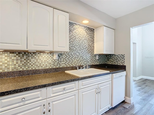 kitchen featuring tasteful backsplash, dark countertops, white cabinetry, a sink, and dishwasher