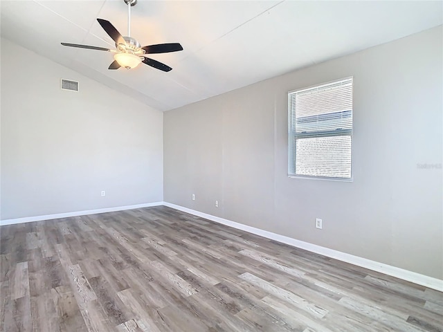 empty room featuring light wood-style floors, visible vents, baseboards, and vaulted ceiling